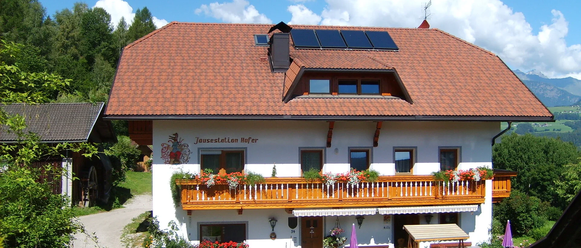 Facciata del maso Hofer Hof con balcone fiorito e pannelli solari sul tetto