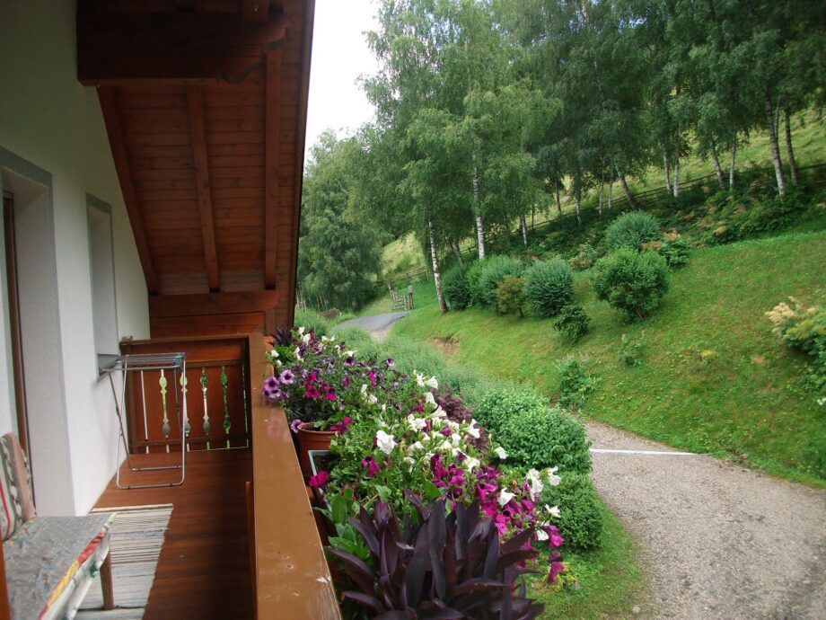 Balcone dell’appartamento Alpenrose con fiori e vista sul bosco