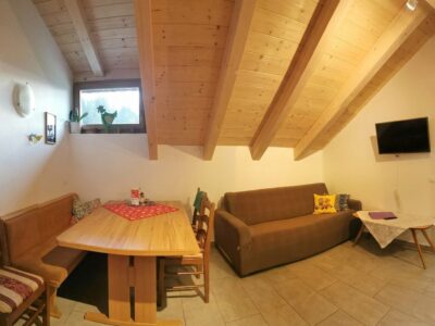 Zona pranzo dell’appartamento Geranie con panca in legno e divano