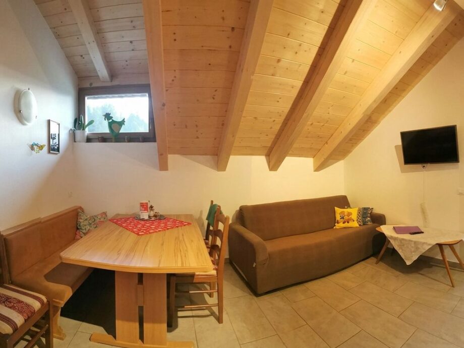 Zona pranzo dell’appartamento Geranie con panca in legno e divano