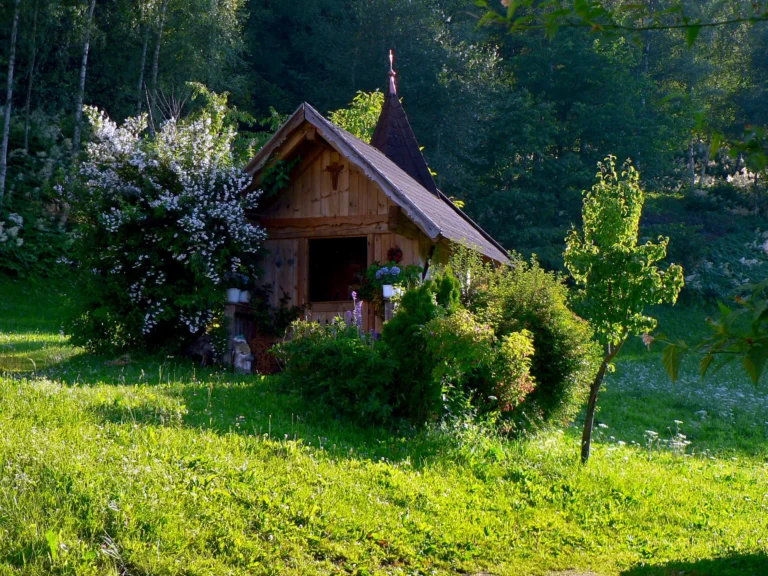 Cappella in legno del maso Hofer Hof fra alberi e fiori