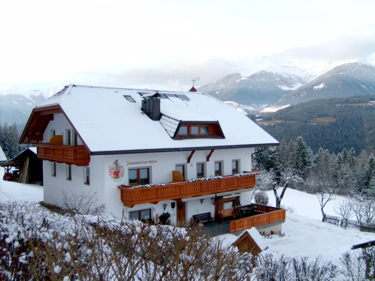 Il maso Hofer Hof coperto di neve con le montagne sullo sfondo