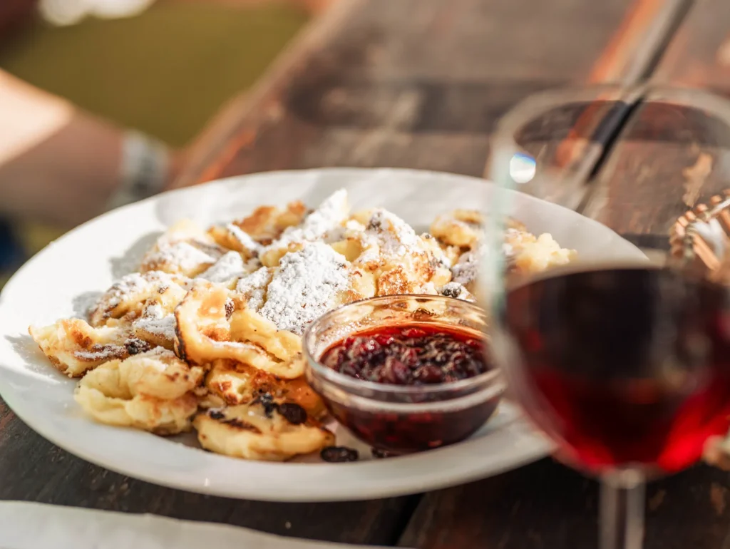 Kaiserschmarrn con zucchero a velo e confettura accanto a un calice di vino rosso