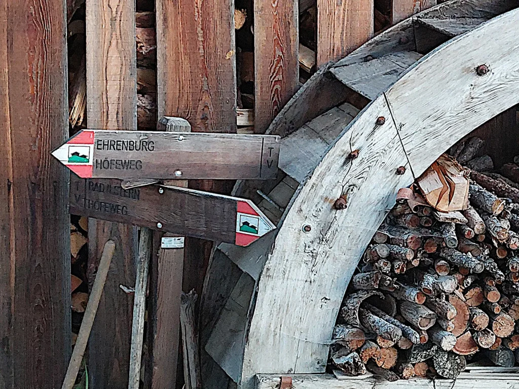 Segnavia Ehrenburg–Höfeweg accanto a una ruota in legno e alla legna accatastata