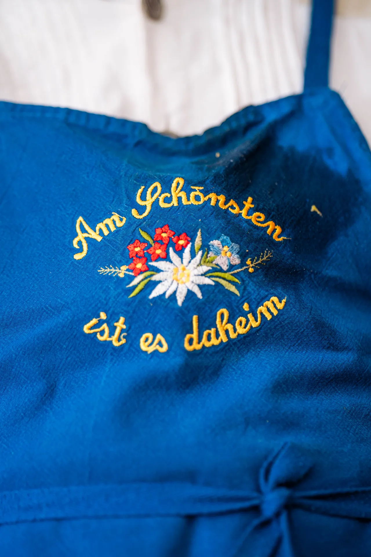 Grembiule blu ricamato con fiori e la scritta Am schönsten ist es daheim